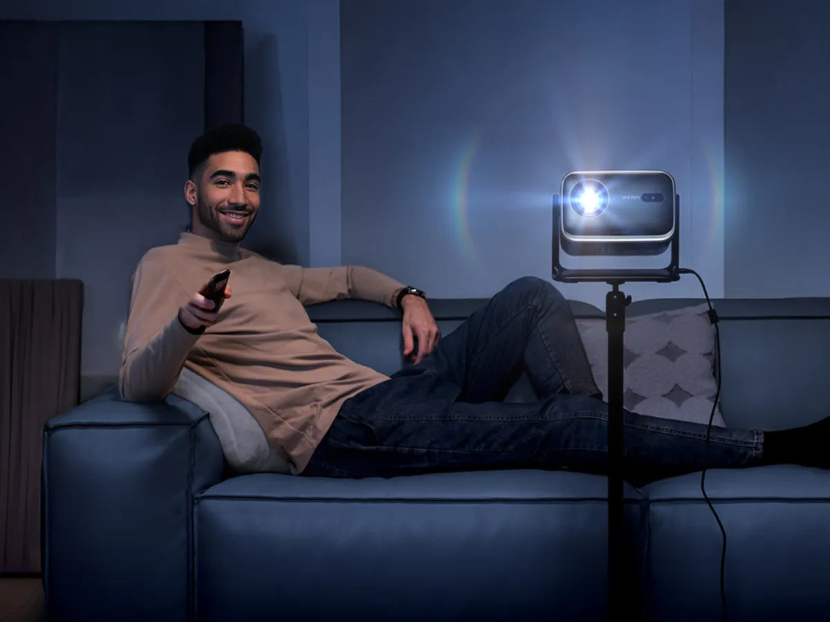 Man sitting on a couch using a portable projector in a dark room.