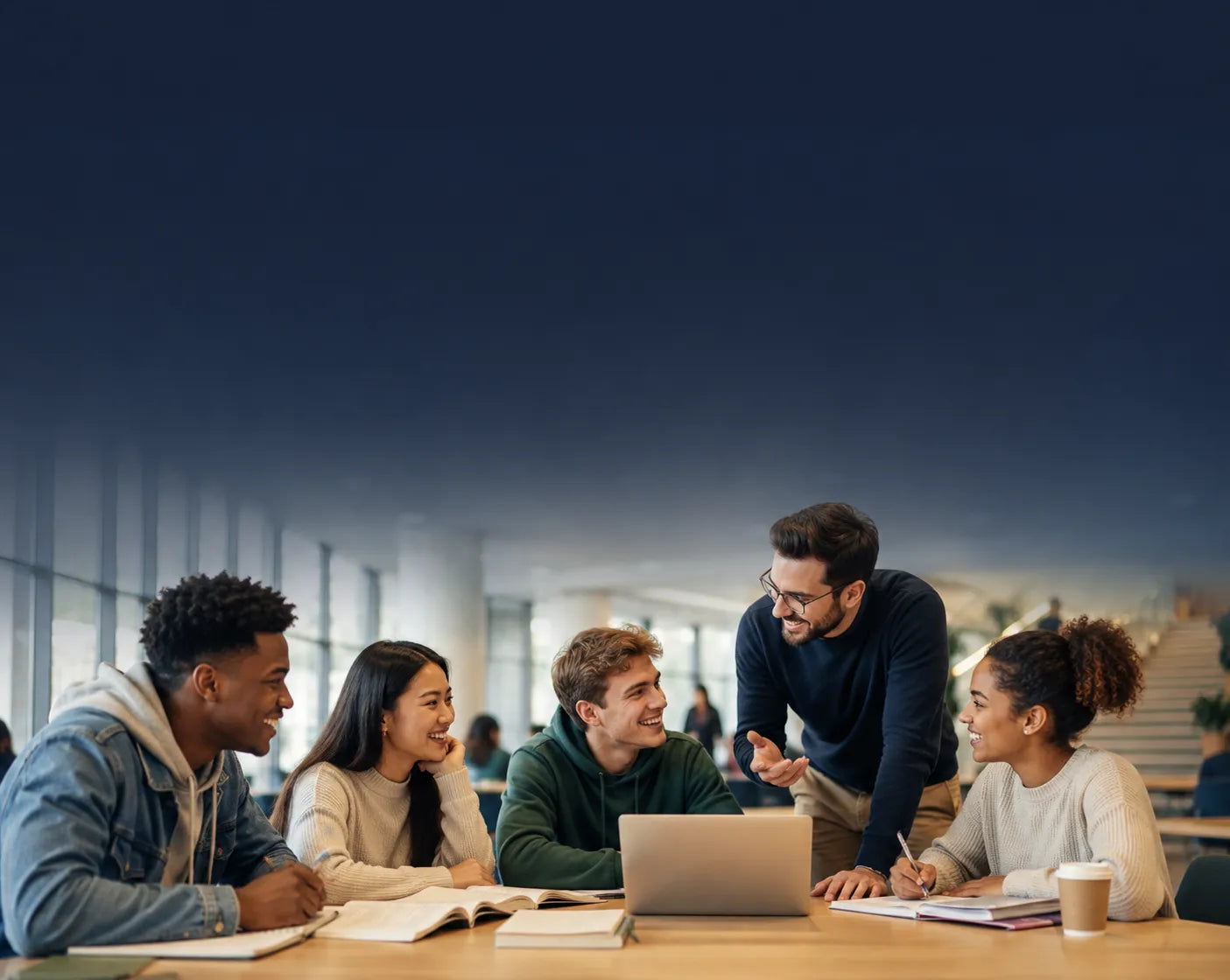 Four young adults collaborating around a table with a laptop in a modern indoor setting, with a dark blue gradient overlay covering the upper portion of the scene.